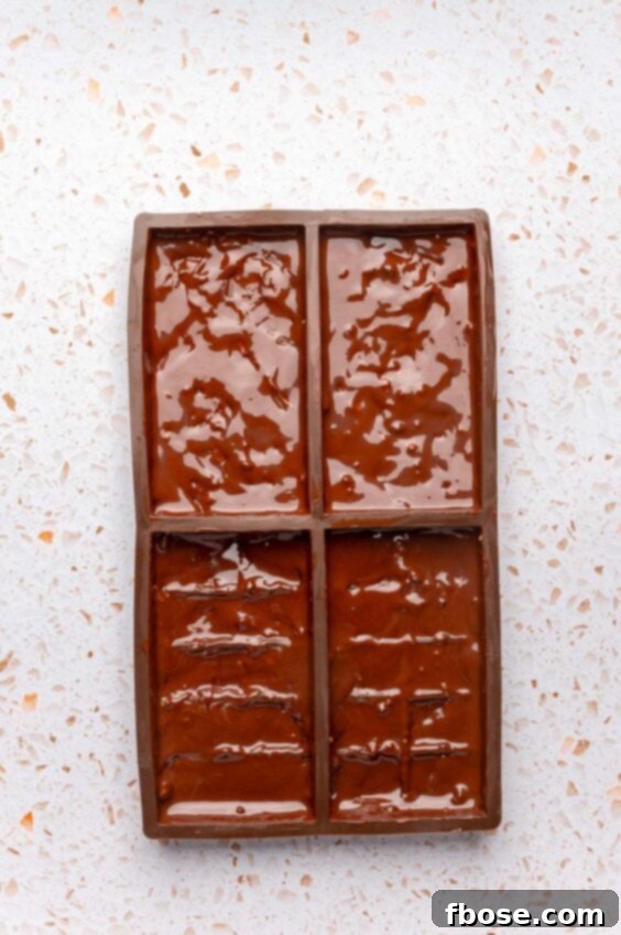 A chocolate bar mold coated with dark chocolate, creating shells for the filling.