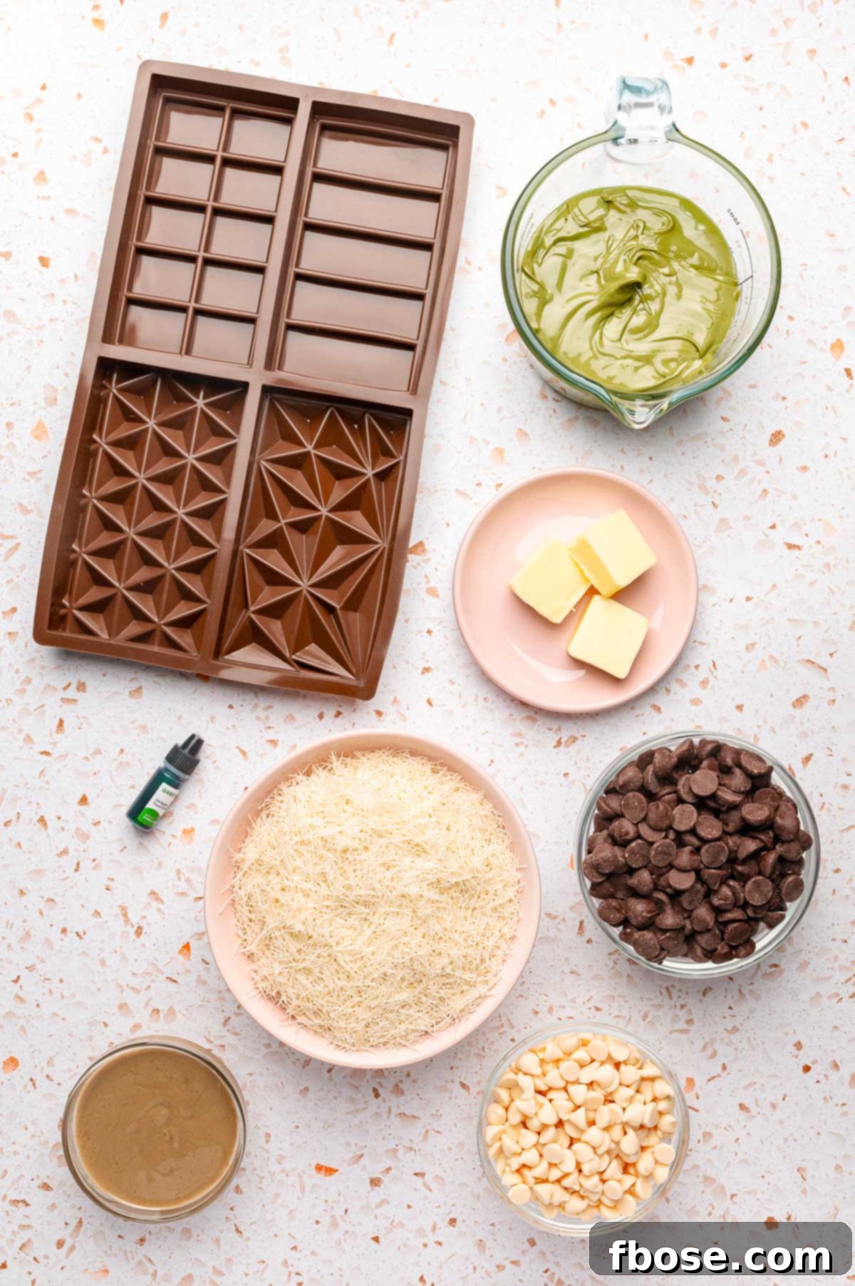 Overhead photo of all the ingredients to make Dubai chocolate bars laid out on a table, including chocolate chips, kataifi, pistachio cream, and tahini.