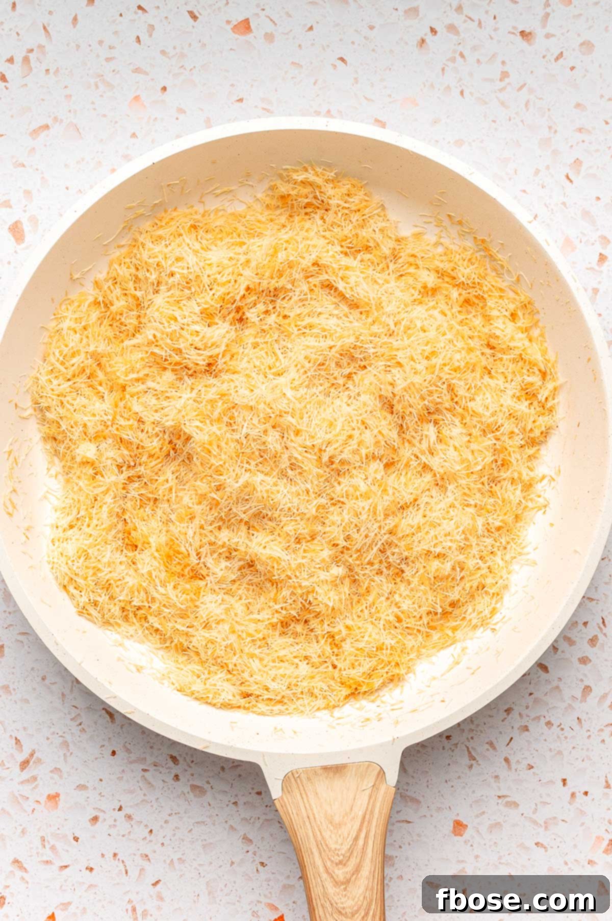 Close up of toasted kataifi dough in a skillet, turning golden brown and crispy.