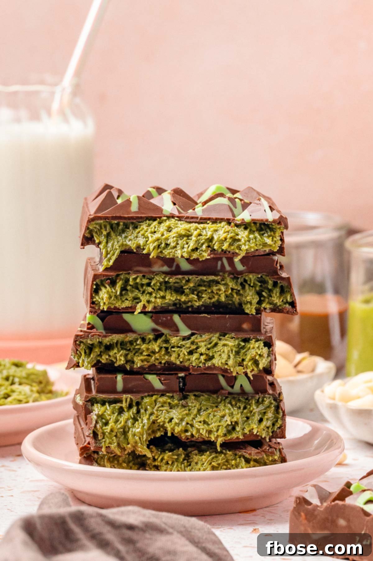 A stack of viral Dubai chocolate bars, broken in half, revealing the green filling on a small pink plate.