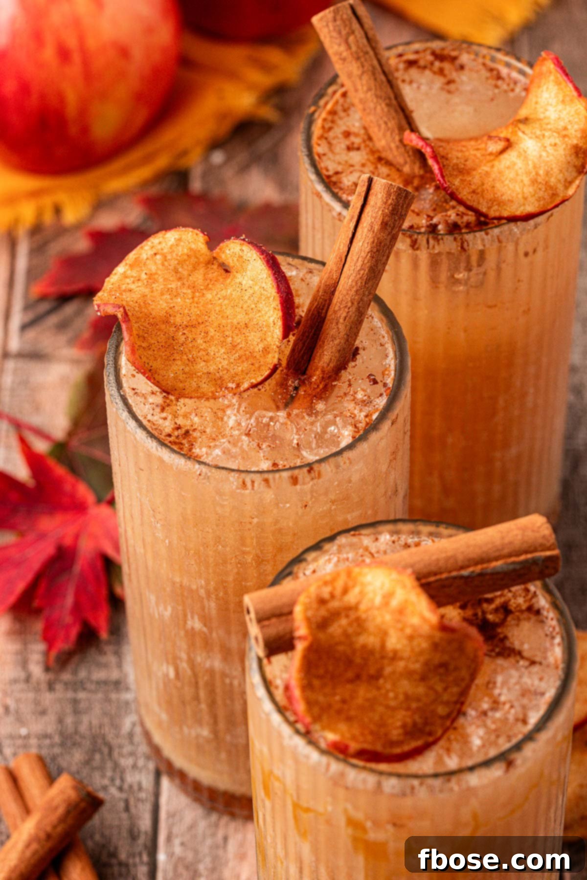 Autumn Crisp Quencher 2 Three apple crisp refresher drinks on a table, garnished with cinnamon sticks and dried apple slices.