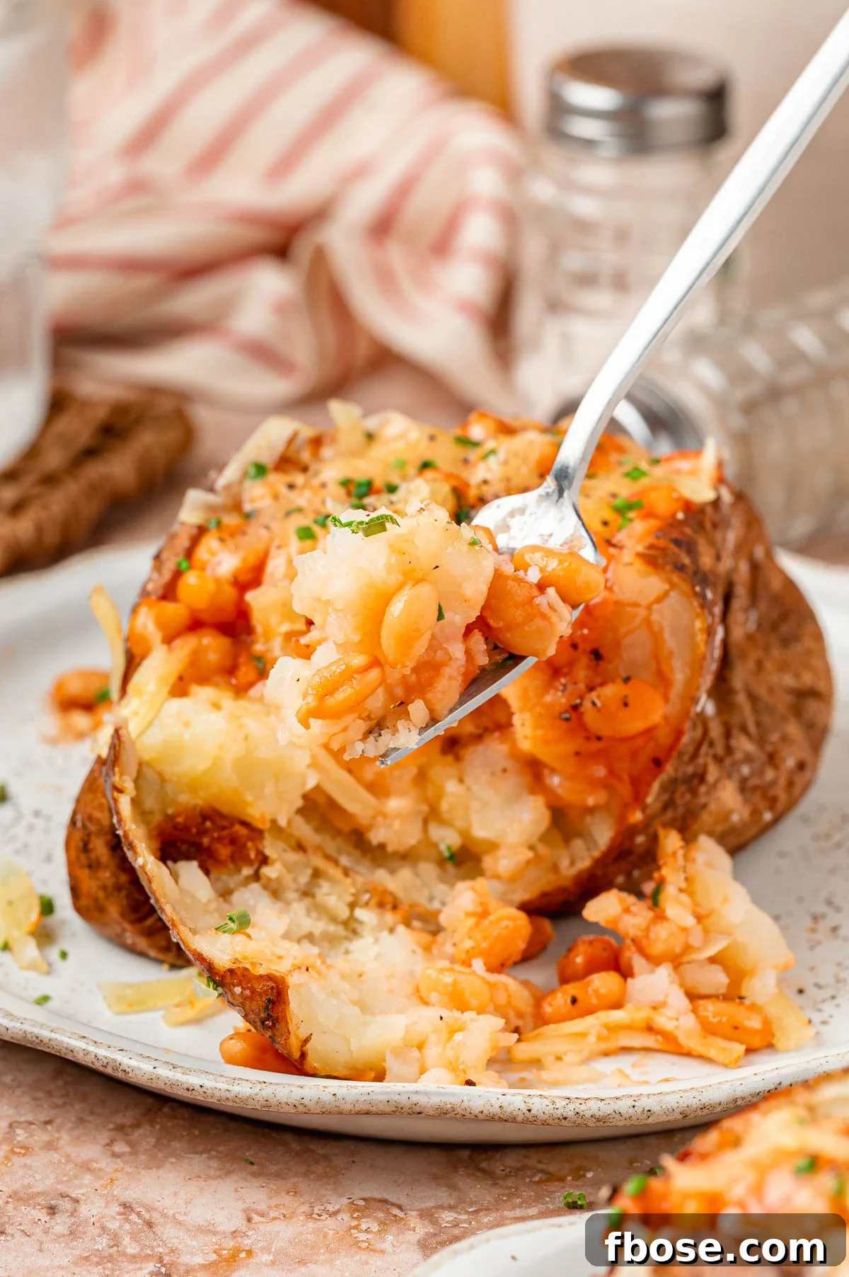 Close up of a fork full of a bite of jacket potato with cheese and baked beans.