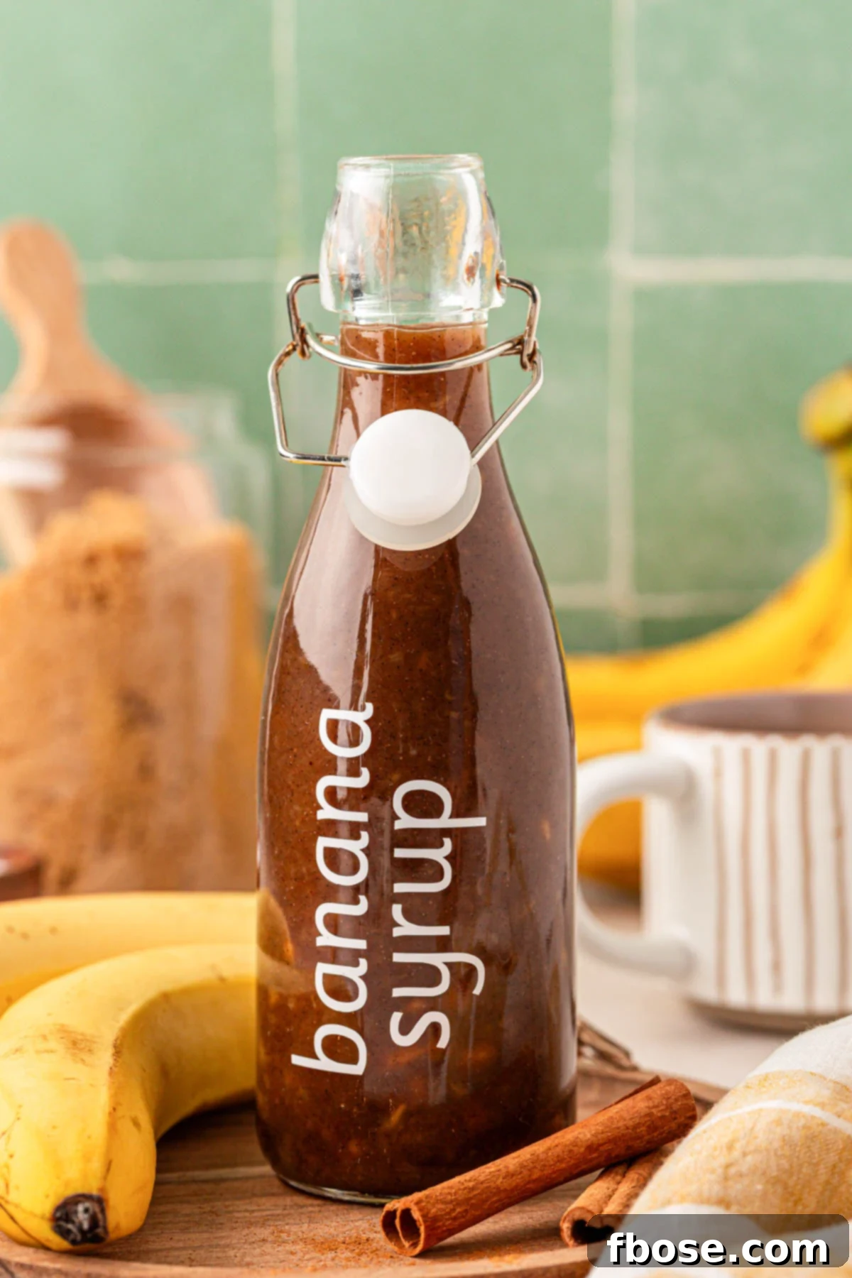 A glass bottle of homemade banana syrup for coffee, with a rich amber color, sitting on a wooden surface.