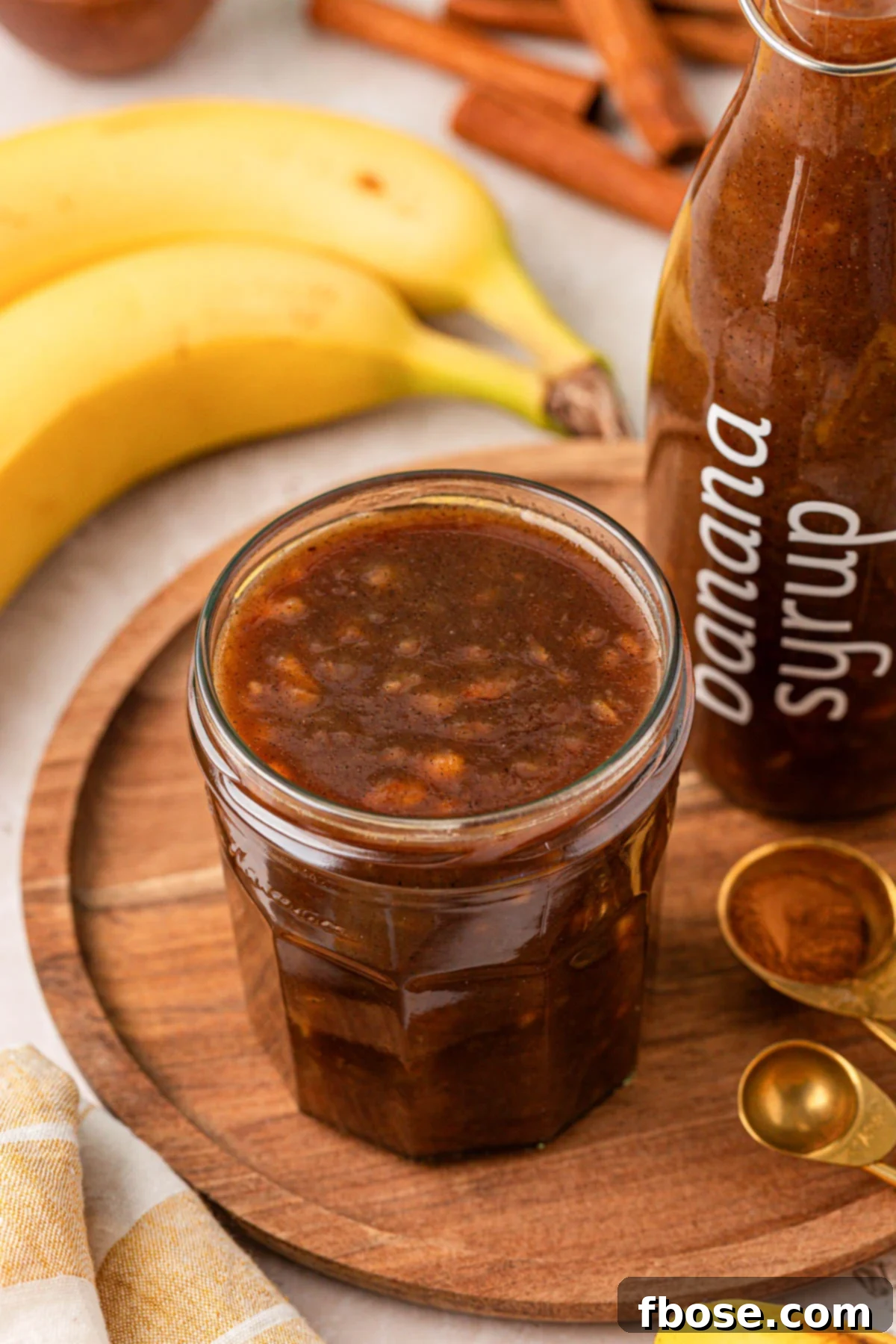 A sealed glass jar of finished banana syrup ready for storage, displayed on a rustic wooden tray.
