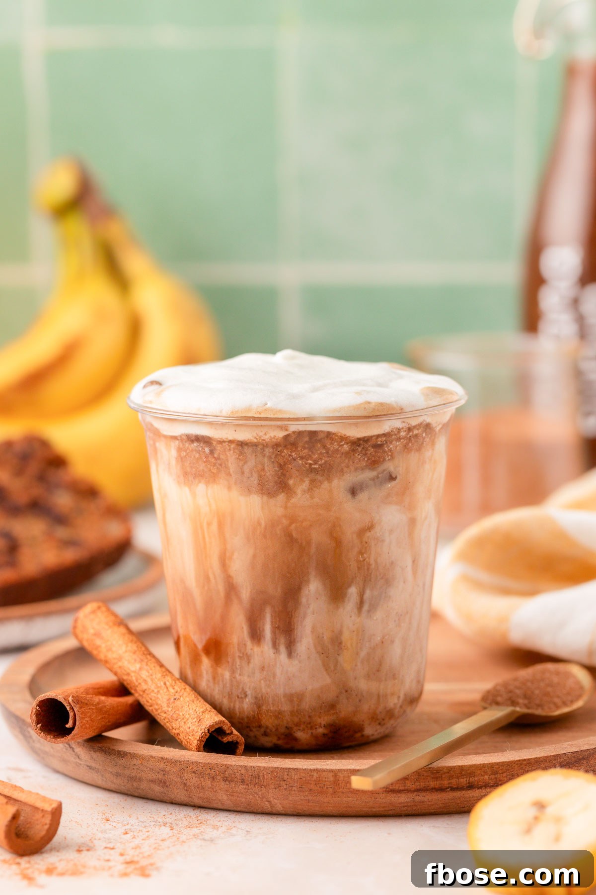 Banana bread latte on a wooden tray with bananas and cinnamon sticks in the background.
