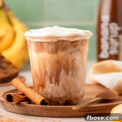 A cup with banana bread latte on a wooden tray.