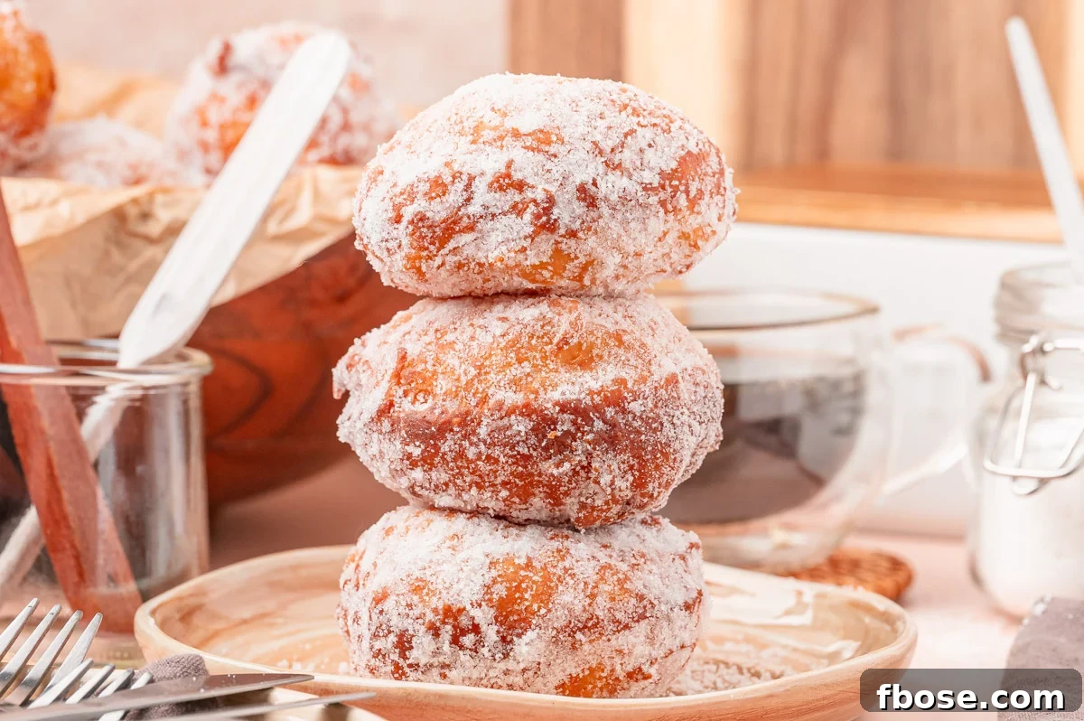 A stack of three malasadas on a tan plate.