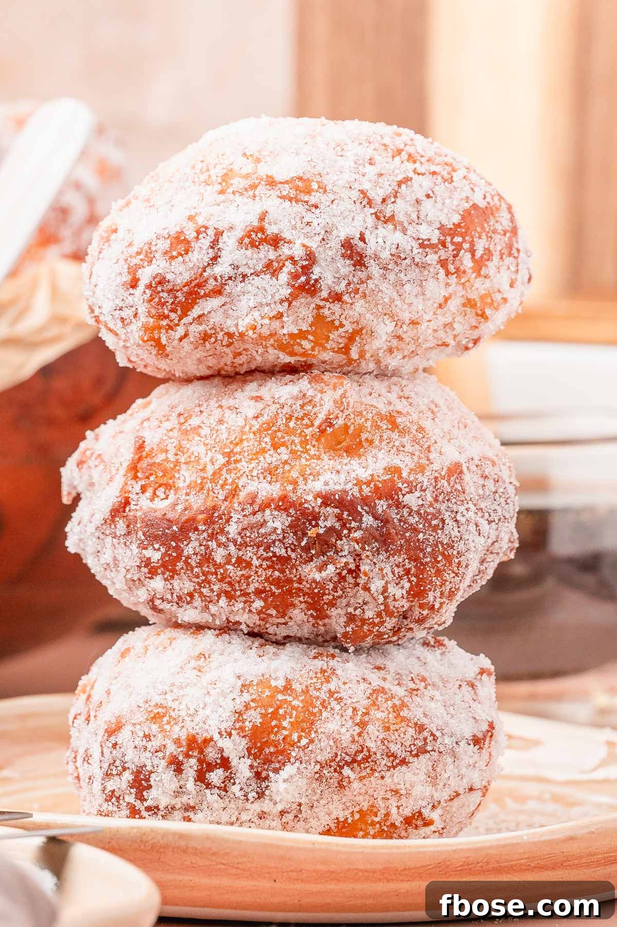 A stack of three malasadas on a tan plate.