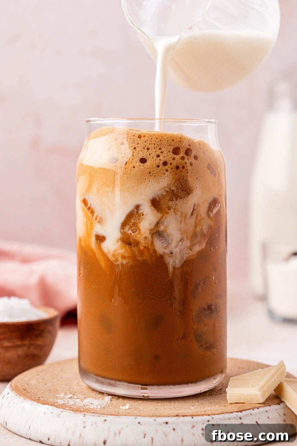 Cream being poured into a glass filled with iced coffee.