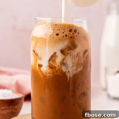 Cream being poured into a glass filled with iced coffee.
